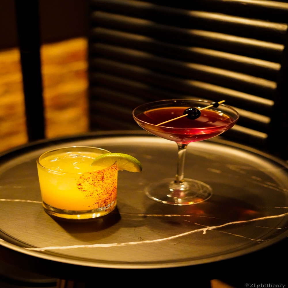Two drinks on a side table by the window blinds